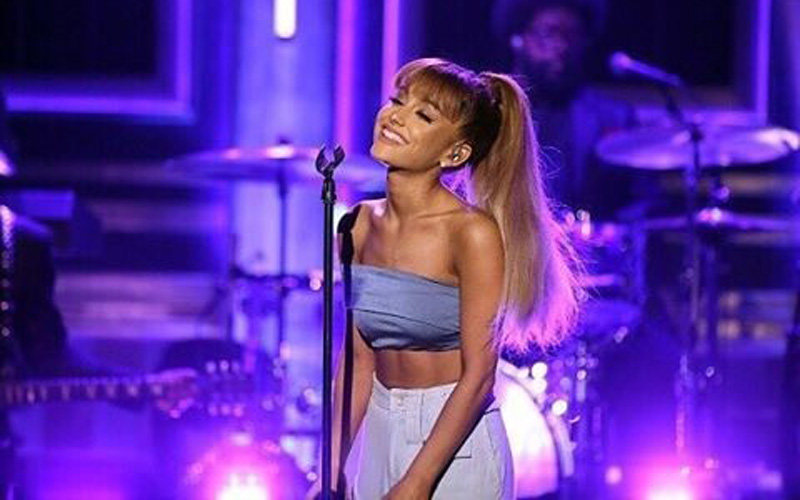 Ariana Grande cantando no palco com fundo roxo