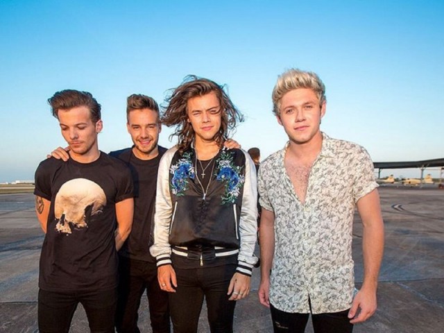 Os quatro integrantes do One Direction lado a lado em fundo de paisagem com céu azul
