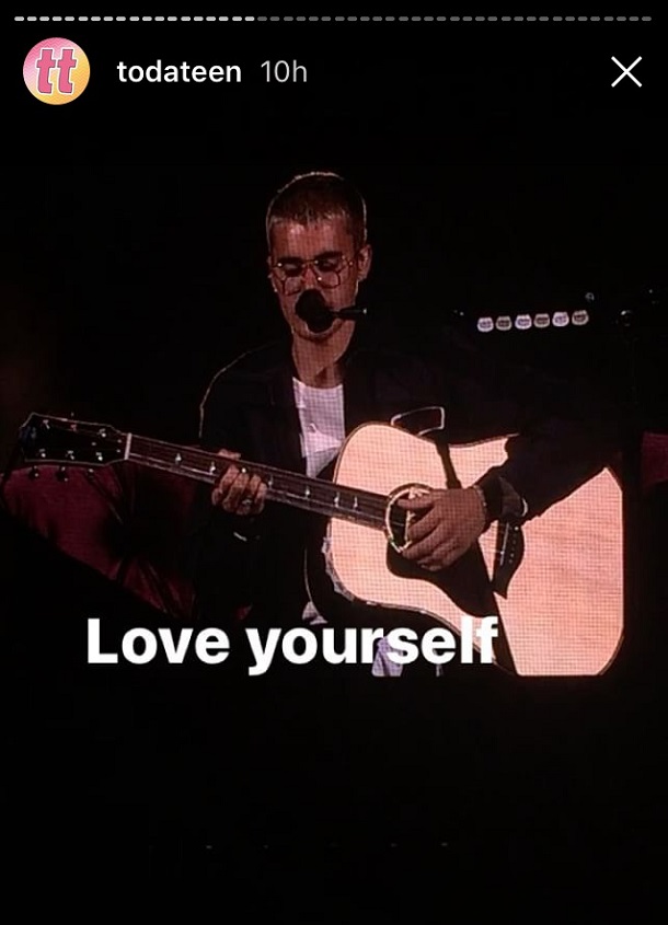 Justin sentado no palco com violão