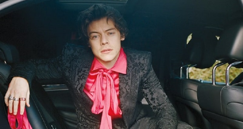 Harry Styles sentado no banco traseiro de um carro usando terno.