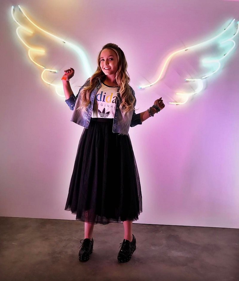 Larissa Manoela encostada numa parede com luminárias que parecem asas de anjo