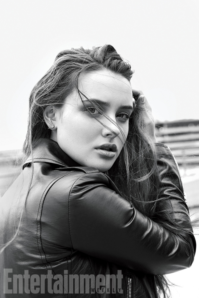 Katherine Langford mexe no cabelo usando jaqueta, em preto e branco