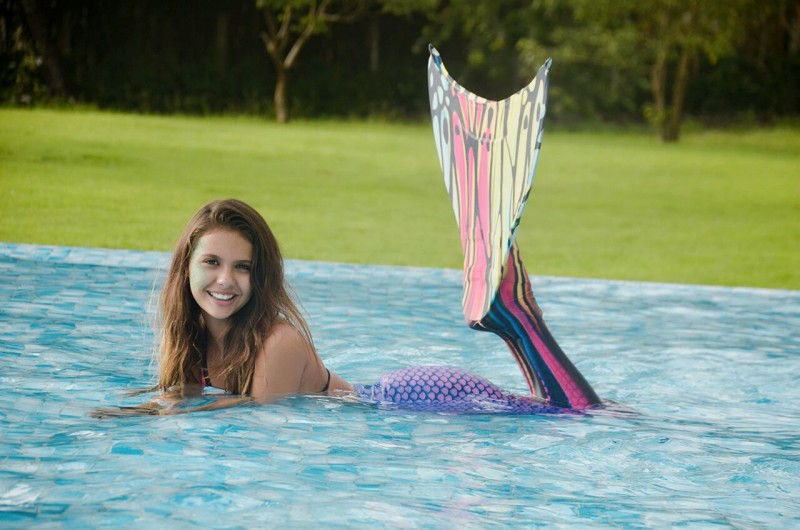 menina usando cauda de sereia posa em piscina