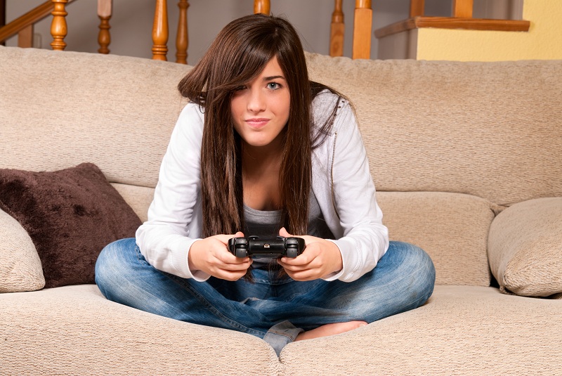 Menina jogando vídeo game de pernas cruzadas no sofá pensando nos canais mais nerds