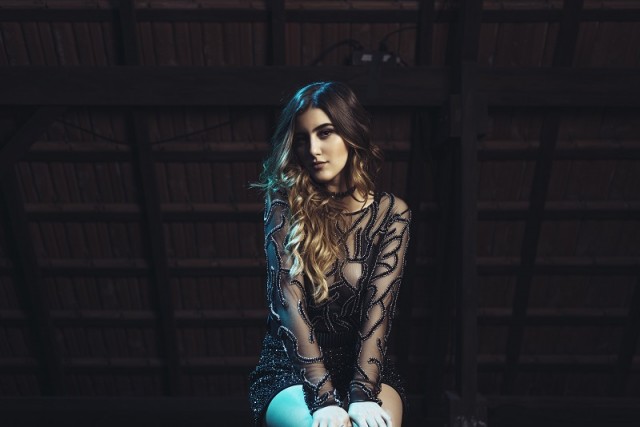 Sofia Oliveira sentada com roupa transparente preta em fundo preto