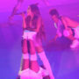 Ariana Grande cantando apoiada em pés de bailarino que está embaixo dela