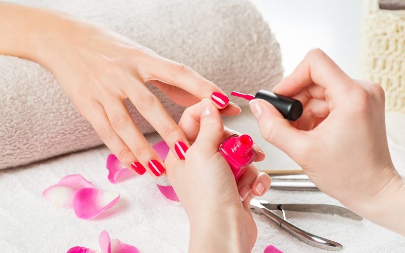 Moça pintando as unhas com a cor de esmalte rosa