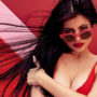 Kylie Jenner com cabelos ao vendo usando óculos vermelho, body vermelho e fundo vermelho