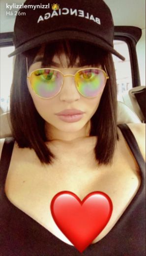 Kylie Jenner usa boné e blusa preta, com o óculos de sol do filho do snapchat e um emoji de coração
