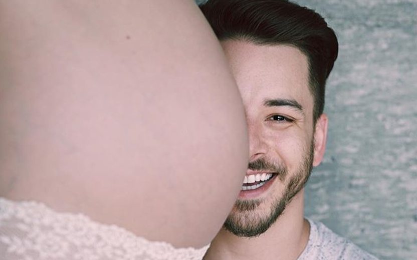 Junior Lima sorrindo ao lado de barriga de sua esposa grávida