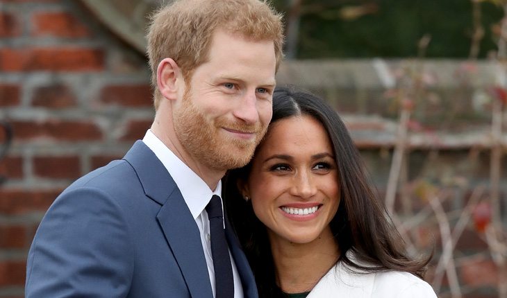 Príncipe Harry e Meghan Markle sorrindo para fotógrafos