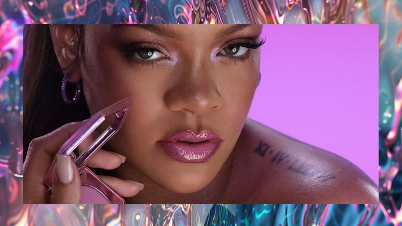 Close-up de Rihanna segurando um blush da Fenty Beauty, com maquiagem em tons de rosa e fundo lilás.